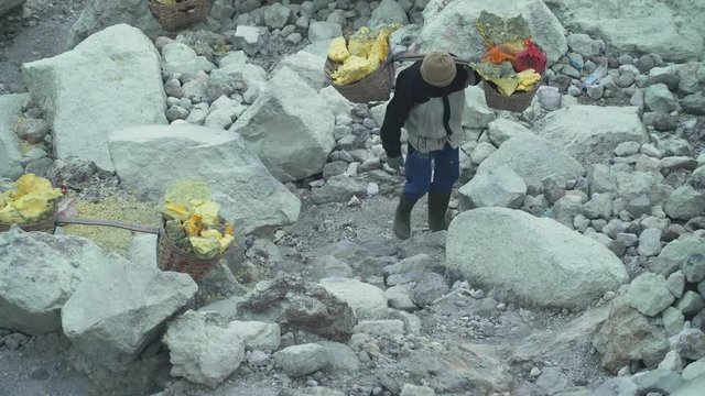 Worker carries a basket with pieces of sulfur on his shoulder. Sulfur miners carries sulfur from inside the crater of Kawah Ijen volcano in East Java, Indonesia.