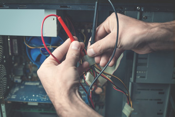 Man checking computer with a multimeter.