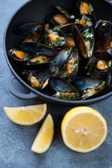 Closeup of a cast-iron pan with boiled mussels and lemon, selective focus, vertical shot