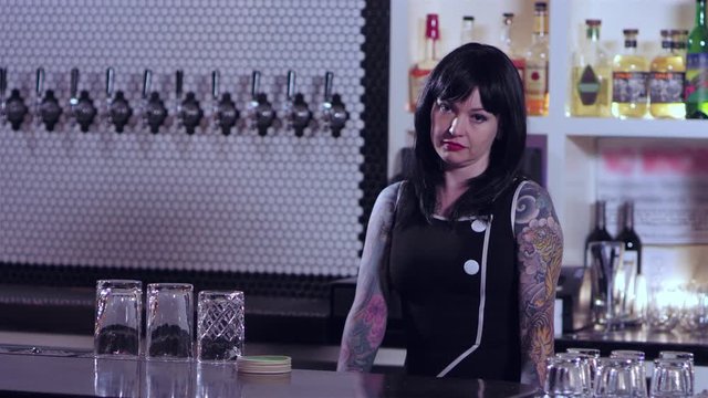Portrait shot of an attractive tattooed bartender lady acting impatient at a bar