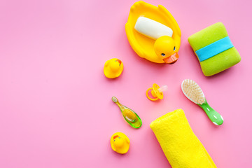 Bath accessories for kids. Yellow rubber duck, soap, sponge, brushes, towel on pink background top view copyspace