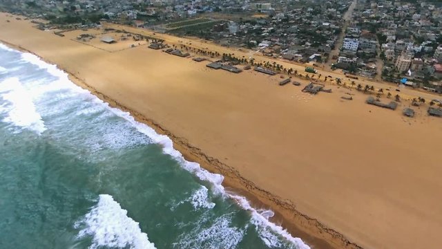 Pan right aerial, waves crash on Cotonou beach