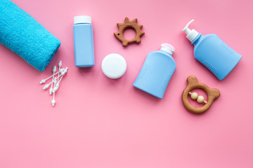 Natural hypoallergenic children's cosmetics. Bottles, towel and toys on pink background top view copyspace