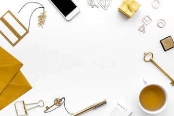 Office desk in trendy gold color. Glittering stationery near cup of tea, cell phone   on white background top view copyspace