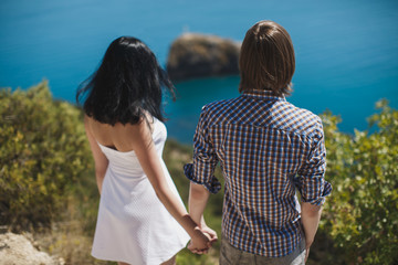 Young couple boy and girl holding hands on a cliff overlooking the sea