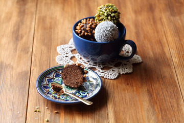 Vegan Chocolate Cake Pops sprinkled with pistachios, walnuts and coconut, in blue cup, on wooden background.
