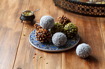 Vegan Chocolate Cake Pops sprinkled with pistachios, walnuts and coconut, on blue plate, on wooden background.