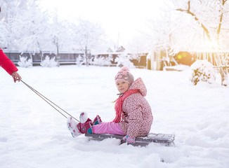 a small child on a sled. girl rolls on snowdrifts in winter, sun shines