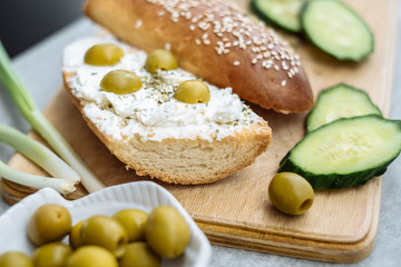 Whole and slice of homemade bread on a wooden board with cream cheese and olives in bowls.