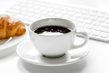 Office lunch with coffee and croissant, keyboard on white table 