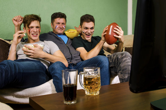 Father and sons sitting in cozy living room and watching american football