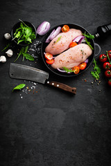 Fresh raw chicken meat, fillet marinated with spices, onion and tomatoes on black background. Top view