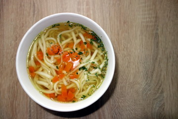 Broth with noodles, carrot and parsley in white bowl on wooden table