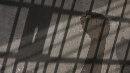African American Man Raised Fist Painted on a Concrete Wall Under Jail Bars Shadow