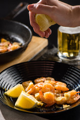 A woman's hand presses a lemon over fried royal prawns