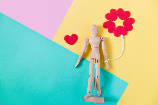 Wooden man figure holding red heart balloon. Wooden human dummy on pink, blue and yellow background with copy space for your text. Concept for valentine's day celebration or couple of love.
