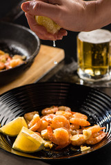 A woman's hand presses a lemon over fried royal prawns
