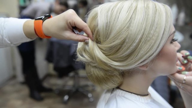 One visagiste makes hairstyle and other paints lips to girl model. Beauty salon - woman doing hair styling and makeup