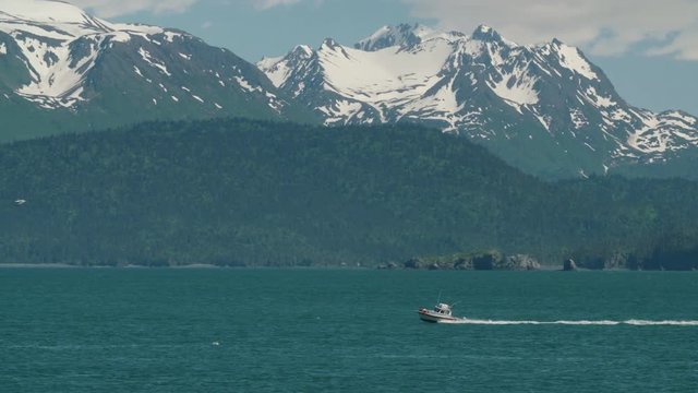 A boat crusing by in the bay with beautiful snow capped mountains in the background