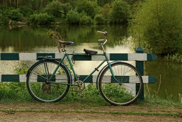 старый велосипед стоит у деревянного ограждения на берегу водоёма