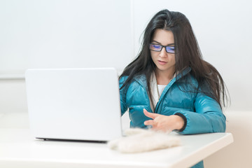 the girl wearing spectacles in casual clothes of mint color works with a laptop on the Internet