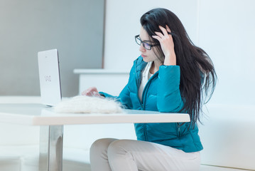 the girl wearing spectacles in casual clothes of mint color works with a laptop on the Internet