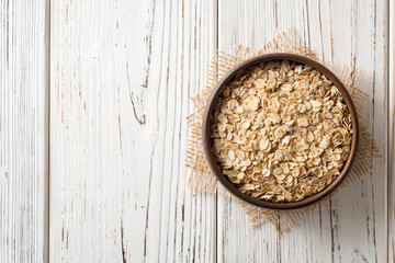 Oat flakes in ceramic bowl on white wooden table