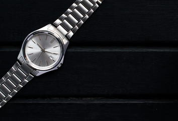 Stainless steel silver mens wrist watch on a black wooden surface, with lots of copy space and contrast - Powered by Adobe