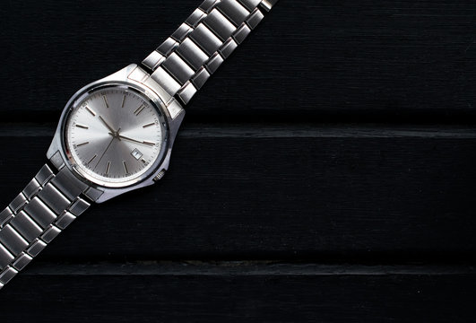 Stainless steel silver mens wrist watch on a black wooden surface, with lots of copy space and contrast