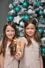 Two girls with sparklers in front of Christmas tree. Selective focus. New Year holidays concept