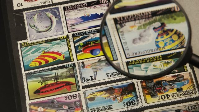 Collector philatelist leafs through the album with a collection of postage stamps and looks  at the stamps through a magnifying glass