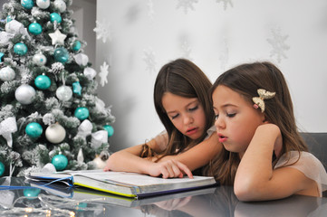 Little girls reading the book next to a Christmas tree. Reading fairy tale for holidays