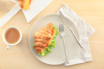 Plate with delicious croissant sandwich on table