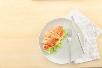 Plate with delicious croissant sandwich on table