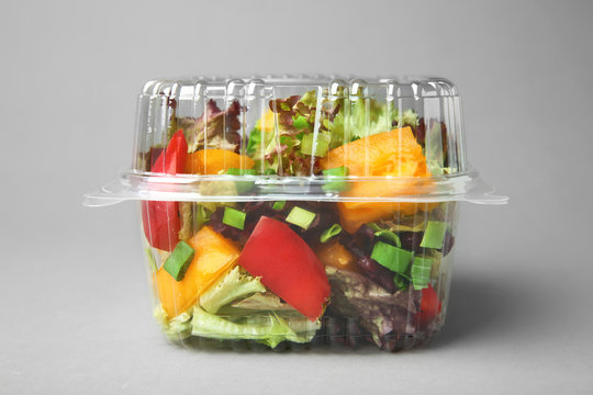 Plastic container with salad on grey background