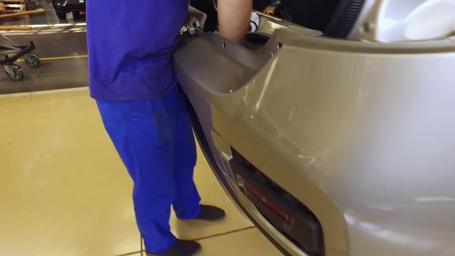 worker is carrying and installing a rear bumper on an auto, walking in a car factory workshop
