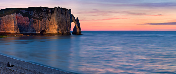West coast of France. Cliffs of Etretat, Lovely couple sitting on the beach and meeting sunset.