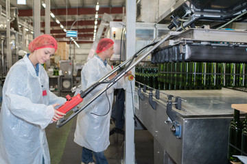 positive winery workers with bottling machinery on factory