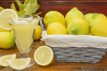 Un jugo de limón natural exprimido y una cesta con limones recien cosechados