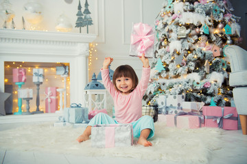 Little baby girl opens New Year gift near Christmas tree