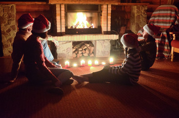 Happy family sitting near fireplace at home and celebrating Christmas and New Year, parents and...