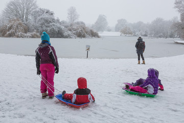 Children on sledges wearing snow suits in the snow facing a frozen lake