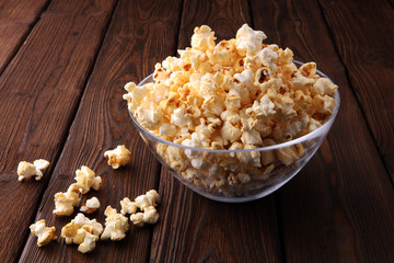 Glass bowl with popcorn on brown wooden background