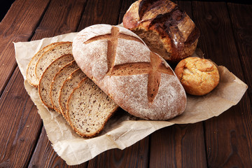 Different kinds of bread and bread rolls on brown wooden table. Kitchen or bakery poster design.