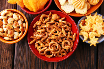 Salty snacks. Pretzels, chips, crackers on brown wooden background