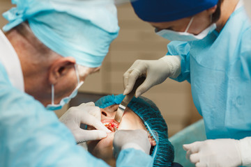 Male old professional dentist surgeon in uniform and female assistant helps to performing operation install dental implant teeth of woman patient in clinic light office with modern tools equipment.