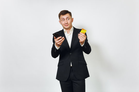 Young Sad Concerned Disquieted Business Man In Black Suit Holding Golden Credit Card, Mobile Phone Isolated On White Background For Advertising. Concept Of Money, Achievement And Wealth In 25-30 Years