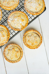 Traditional British Christmas Sweet Pastry Home Baked Mince Pies with Apple Raisins Nuts Filling on Cooling Rack. Golden Shortcrust Powdered White Plank Wood Table Top View Copy Space