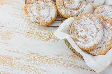 Traditional Spanish or Philippine Pastry Ensaimada. Powdered on Cooling Rack and in Wicker Basket. White Wood Table. Cozy Rustic Kitchen Interior Copy Space.