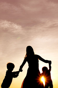 Silhouette of Happy Mother and Little Children Dancing Outside at Sunset